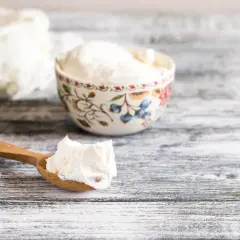 Ein Holzlöffel mit cremigem Quark, daneben eine Schale. Die Frage "wieviel Quark am Tag" beschäftigt viele.
