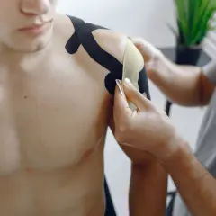 Fizjoterapeuta okleja taśmą bark mężczyzny, łagodząc ból barku po laparoskopii.