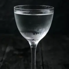 Szklanka z mroźną wódką, pokryta kroplami kondensacji, na ciemnym tle.