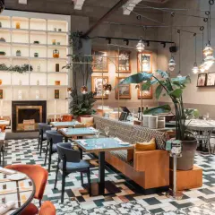 Interni eleganti di locali trendy a Milano, con tavoli apparecchiati, sedute comode e un camino decorativo.