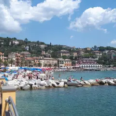 Plage animée à Santa Margherita Ligure, Italie, avec des parasols colorés, des baigneurs sur les rochers et des bâtiments pittoresques à flanc de colline.
