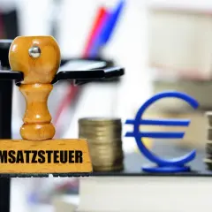Stempel mit "Umsatzsteuer" und Euro-Symbol, Münzstapel und Bücher. Symbolisiert die regelbesteuerung landwirtschaft.