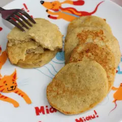 Placki bananowe na talerzu z kotkiem i pieskiem. Jeden placek jest rozkrojony widelcem.