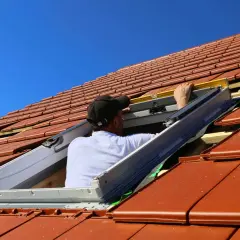Monter montuje okienko w dachu, używając poziomicy.