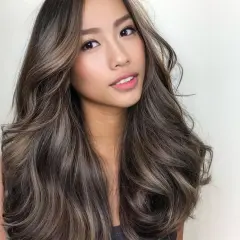 Mujer con cabello castaño con reflejos claros, ondulado y brillante. Descubre cómo dar brillo al pelo teñido para un look radiante.