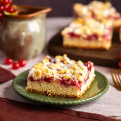 Saftiger Johannisbeerkuchen, wie ihn Landfrauen backen, mit Streuseln und Zuckerguss. Ein Stück auf grünem Teller, daneben rote Johannisbeeren.