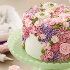 En tårta täckt av vackra blommor skapade genom att spritsa tårta med frosting i rosa, lila och gröna nyanser.