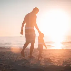Ojciec prowadzi za rękę swoje dziecko 4 lata, spacerując po plaży o zachodzie słońca.