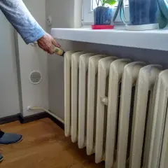 Mężczyzna reguluje termostat na grzejniku, szukając **ekonomicznego ogrzewania mieszkania w bloku**.