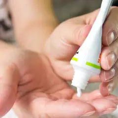 Dłoń wyciska maść z arniki na twarz. Krem delikatnie spływa na otwartą dłoń, gotowy do aplikacji.