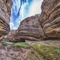 Sendero entre imponentes rocas erosionadas, con el cielo azul y nubes blancas asomando. Un paisaje que evoca la grandeza de los Picos de Urbión.