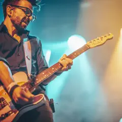 Muzyk w okularach gra na gitarze, otoczony światłami sceny. Jego gra to prawdziwa **farben lehre** dźwięków i emocji.