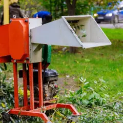 Pomarańczowy rębak z silnikiem spalinowym, gotowy do rozdrabniania gałęzi. To urządzenie, które ułatwia pracę w ogrodzie.