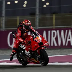 Piloto de MotoGP con traje rojo y casco a juego, en plena carrera. Busca sumar puntos en la clasificación.