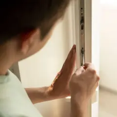 Mężczyzna dokonuje regulacji drzwi balkonowych uchylnych, dokręcając śrubę śrubokrętem.