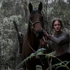 Kobieta z zakrwawioną twarzą i koniem w lesie. W tle widać strzelbę, jakby z opowieści o "Nightingale".