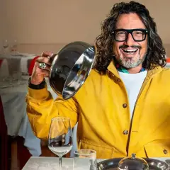Chef con giacca gialla solleva un coperchio, pronto a svelare un piatto in un ristorante. Un assaggio di "4 ristoranti".