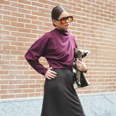 Mujer con gafas naranjas y blusa color burdeos, posando con un bolso de pelo.