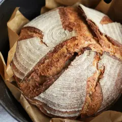 Ein frisch gebackenes Sauerteigbrot mit knuspriger Kruste liegt in einem Gusseisentopf. Perfekt für dein Sauerteigbrot Rezept!