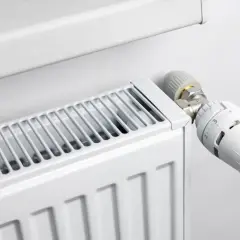 Biały grzejnik z widoczną głowicą termostatyczną, która pozwala regulować temperaturę. Różne rodzaje głowic termostatycznych zapewniają komfort cieplny.