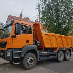 Pomarańczowa wywrotka, idealna do transportu materiałów budowlanych. Z kategorią C można ciągnąć taką przyczepę.