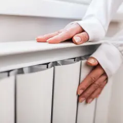 Dłonie na grzejniku, sprawdzające temperaturę. Czas pomyśleć, kiedy wyłączyć ogrzewanie podłogowe.