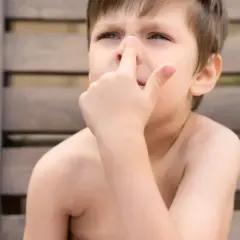 Niño con dedo en la nariz, quizás pensando en comerse los mocos.
