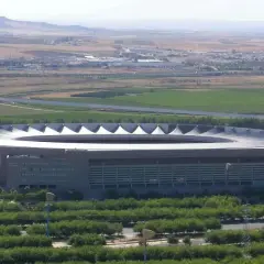 Imponujący stadion La Cartuja otoczony zielenią, z widokiem na pola i miasto w oddali.
