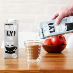 Ręka wylewa mleko dla baristów Oatly do szklanki. Obok stoi karton tego samego napoju.