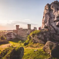 Skały i ruiny zamku na Jurze Północnej. Wspinacze zdobywają skalną ścianę, a w tle widać zamek.