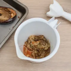 Berenjenas asadas en una bandeja, listas para convertirse en un delicioso hummus de berenjena. Un batidor de mano espera para mezclar.