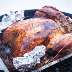 Ein goldbrauner truthahn im backofen, bereit zum Servieren. Die Haut ist knusprig und glänzend, mit Folie an den Flügelspitzen geschützt.