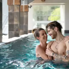Para w basenie SPA, uśmiechnięci, patrzą na siebie.