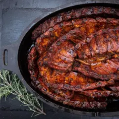 Saftige spareribs im Dutch Oven, glasiert und bereit zum Genießen. Ein Rosmarinzweig liegt daneben.