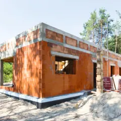 Budowa domu z pustaków ceramicznych. Widać fundamenty, ściany z otworami okiennymi i drzwiowymi. To początek realizacji projektów domów bez pozwolenia.