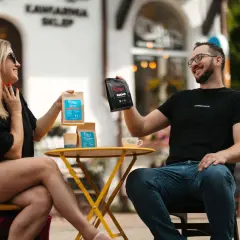 Para, która cieszy się najlepszą kawą ziarnistą nie kwaśną, prezentuje opakowania z kawą na tle kawiarni.