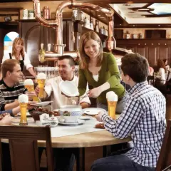 Gäste genießen Bier und Essen im Erdinger Brauhaus. Eine Kellnerin serviert, während Freunde lachen und trinken.