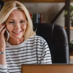 Uśmiechnięta blondynka w okularach rozmawia przez telefon, szukając pożyczki na telefon od zaraz.
