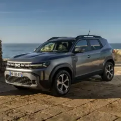 Nowy Dacia SUV na tle kamiennego muru i morza.