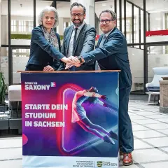 Drei Personen legen ihre Hände auf ein Banner für ein berufsbegleitendes Studium in Leipzig.