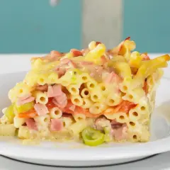 Ein Stück saftiger Makkaroni Auflauf mit Schinken, Gemüse und Käse, serviert auf einem weißen Teller.