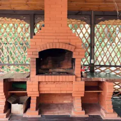 Solidny, prosty grill z cegły w altanie. Obok dwa czerwone gaśnice.