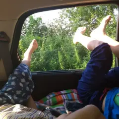 Dzieci śpią w samochodzie, wystawiając nogi przez okno. Wentylacja działa, a za oknem bujna zieleń.