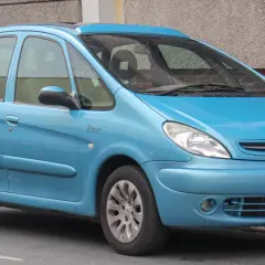 Błękitny Citroen Xsara Picasso z napisem "Picasso" na błotniku, zaparkowany przy ceglanej ścianie.