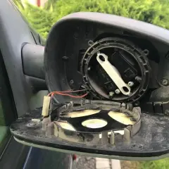 Rozmontowane lusterko zewnętrzne samochodu, gotowe do wymiany. Widać mechanizm regulacji i przewody.