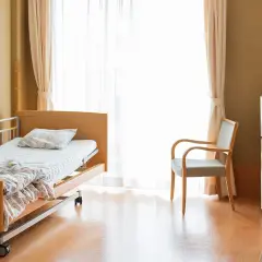 Ein helles Zimmer mit einem Pflegebett auf Rezept AOK, einem Sessel und einem Fernseher.