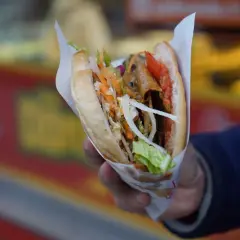 Kebab w bułce z warzywami i mięsem, trzymany w dłoni.