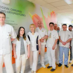Grupa lekarzy i pielęgniarek w białych fartuchach stoi w szpitalnym korytarzu.