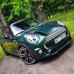 Zielony Mini Cooper na leśnej drodze. Wiele osób chwali sobie ten model, a jego opinie są zazwyczaj pozytywne.
