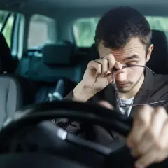Hombre cansado al volante, se frota los ojos. Para evitar la fatiga en la conducción conviene descansar.